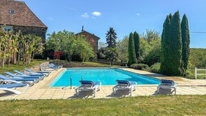 Ein Swimmingpool mit Liegestühlen, umgeben von Grünflächen und einem Steinhaus.