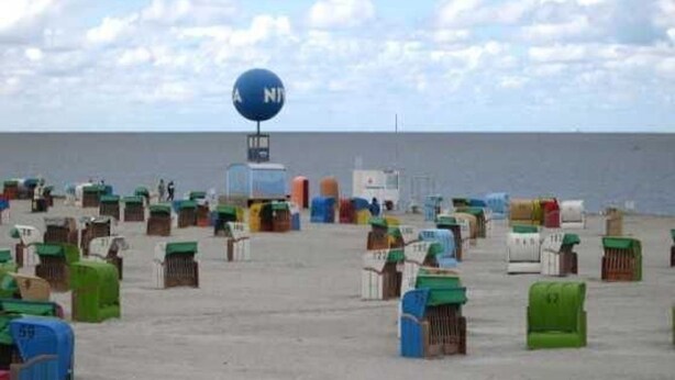 Ein Strand mit vielen nummerierten Behältern, einem großen blauen Schild und blauem Himmel.