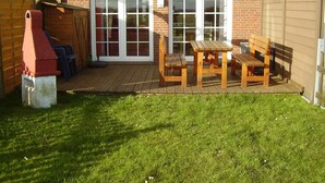 Eine Terrasse mit Holztisch und -bänken, einer Ziegelwand und einem Holzzaun.