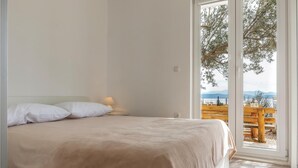 Une chambre à coucher comprenant un lit, une table de chevet, une lampe et donnant sur un espace extérieur avec un banc en bois et une table.