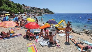 Une plage bondée, où l’on voit des gens bronzer, des parasols et des bateaux.