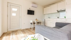Un espace de vie compact comprenant un coin cuisine, un canapé gris, une petite table à manger avec des chaises et une porte blanche.