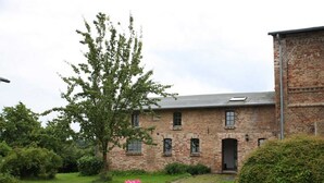 Un bâtiment en briques à l’architecture traditionnelle, un chemin bordé de pierres et un jardin agrémenté de fleurs roses.