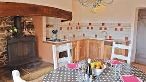 A cozy kitchen with a stone fireplace, a wooden table set for dining, and a tiled backsplash. - Cozy home in Plogastel St Germain with WiFi (Plogastel St Germain)