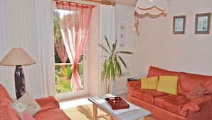 A living room with a sofa, a table, a lamp, a plant, and a window with curtains. - Cozy home in Plogastel St Germain with WiFi (Plogastel St Germain)