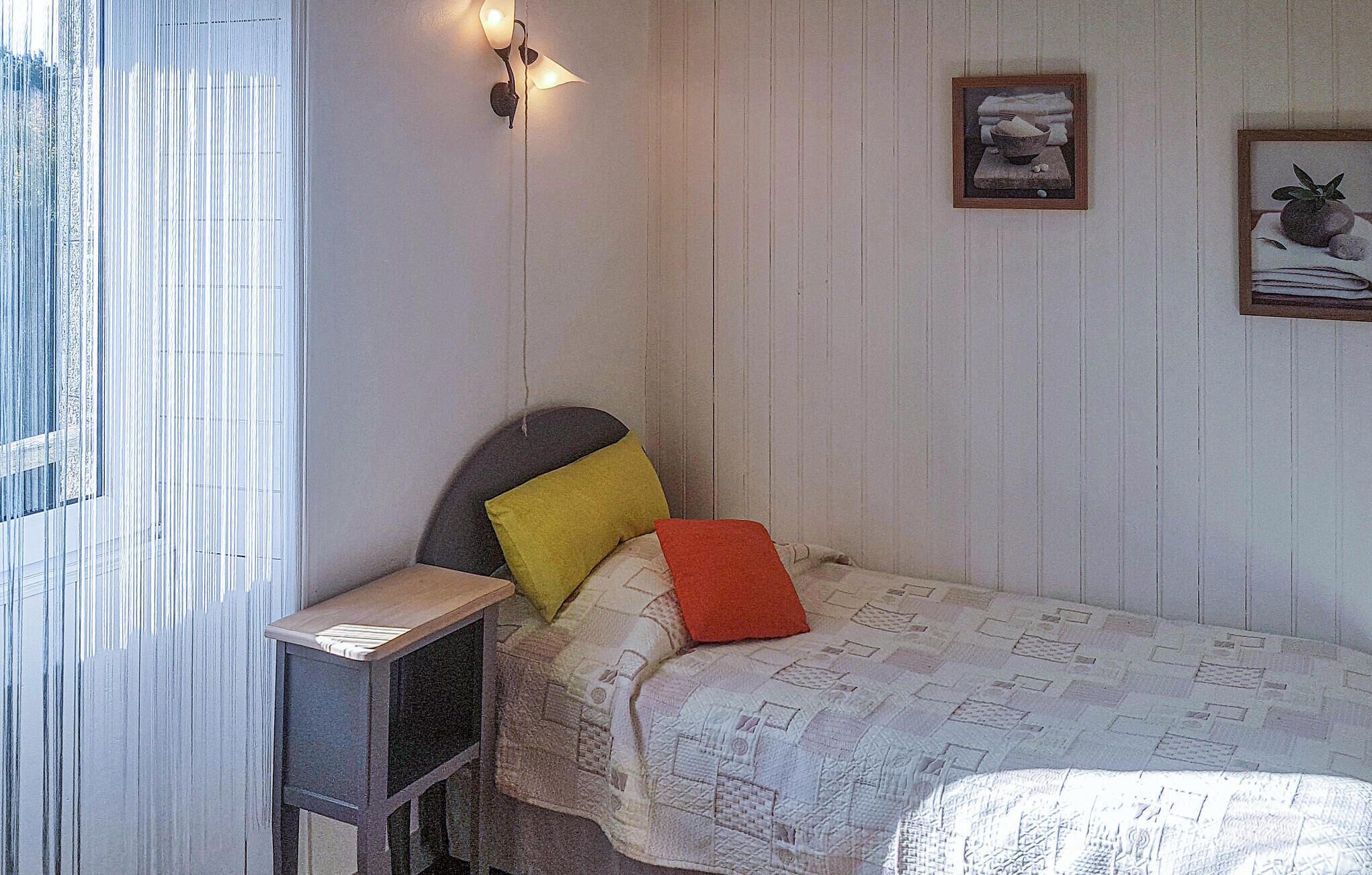 Een knus kamertje met een enkel bed, een nachtkastje en een wandlamp.