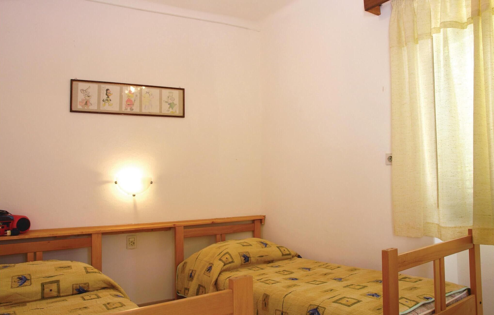 A small, simple room with two wooden beds, a wall-mounted light, and a framed picture.