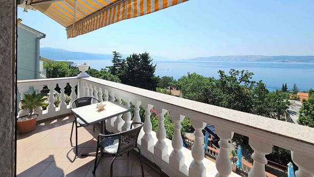 Un balcon agrémenté d’un auvent rayé, avec une table et des chaises, offrant une vue panoramique sur une étendue d’eau et des montagnes lointaines.