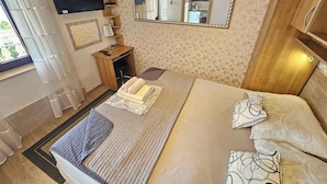 Une chambre à coucher avec un lit, un bureau, une chaise, une télévision, un miroir et une fenêtre.