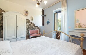 Une chambre à coucher avec un lit, une chaise, une armoire, un mur en pierre et une fenêtre avec des rideaux.