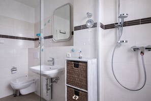 A bathroom with a toilet, sink, mirror, shower, and a decorative basket.