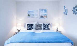 A bed with a blue blanket, white bedding, and nautical-themed pillows.