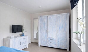 A bedroom with a bed, a wardrobe, a television, a window with a plant, and a mirror.