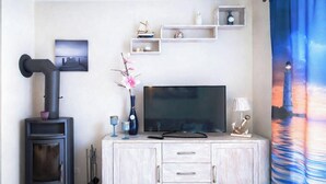 A living room with a fireplace, a flat-screen TV, a cabinet with drawers, and a wall-mounted shelf with decorative items.