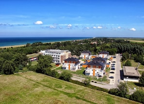 A coastal hotel with multiple buildings, a parking area, and a view of the sea.