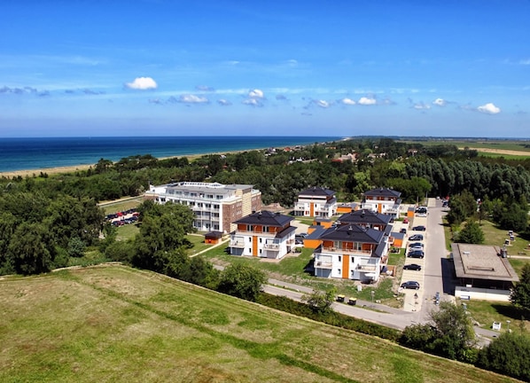 Un hotel costero con varias edificaciones, un estacionamiento y vista al mar.