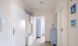 Un pasillo con una puerta a la izquierda, un interruptor de luz, un teléfono y un armario con un espejo y un estante pequeño.