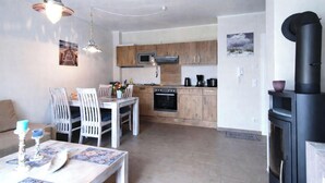 A modern kitchen with wooden cabinets, a microwave, and a stove. There is a dining area with a table and chairs, and a fireplace on the right.