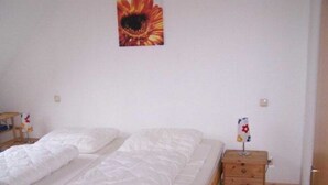 A bedroom with a bed, a wooden nightstand, and a wall-mounted painting. - (225/2) 2-room apartment-Strandstrasse - apartment house Strandburg (Kühlungsborn)