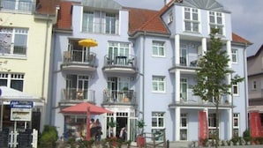 A multi-story building with balconies, a ground-level shop, and a red umbrella. - (225/2) 2-room apartment-Strandstrasse - apartment house Strandburg (Kühlungsborn)