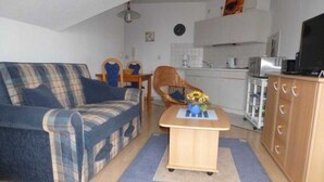 A compact living space with a sofa, a small table with a vase, a chair, and a kitchenette in the background. - (225/2) 2-room apartment-Strandstrasse - apartment house Strandburg (Kühlungsborn)