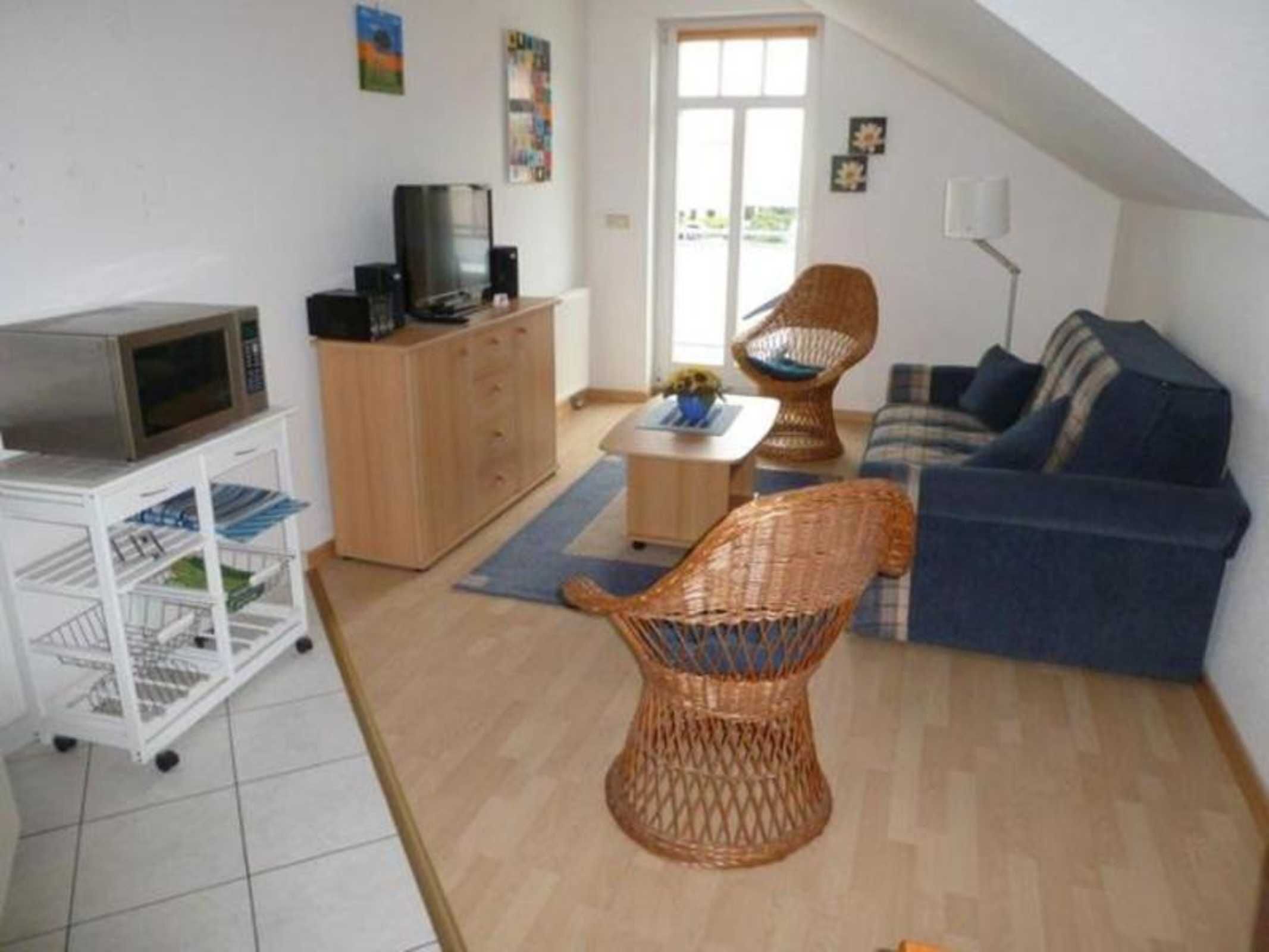 Un salon comprenant un téléviseur, un fauteuil en osier, un canapé et un meuble de rangement blanc.