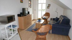 A living room with a television, a wicker chair, a sofa, and a white storage unit. - (225/2) 2-room apartment-Strandstrasse - apartment house Strandburg (Kühlungsborn)