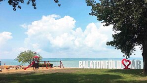 Ranta, jossa on leikkipaikka, kyltti, jossa lukee ”BALATONFÜLÖR”, ja näkymä merelle.