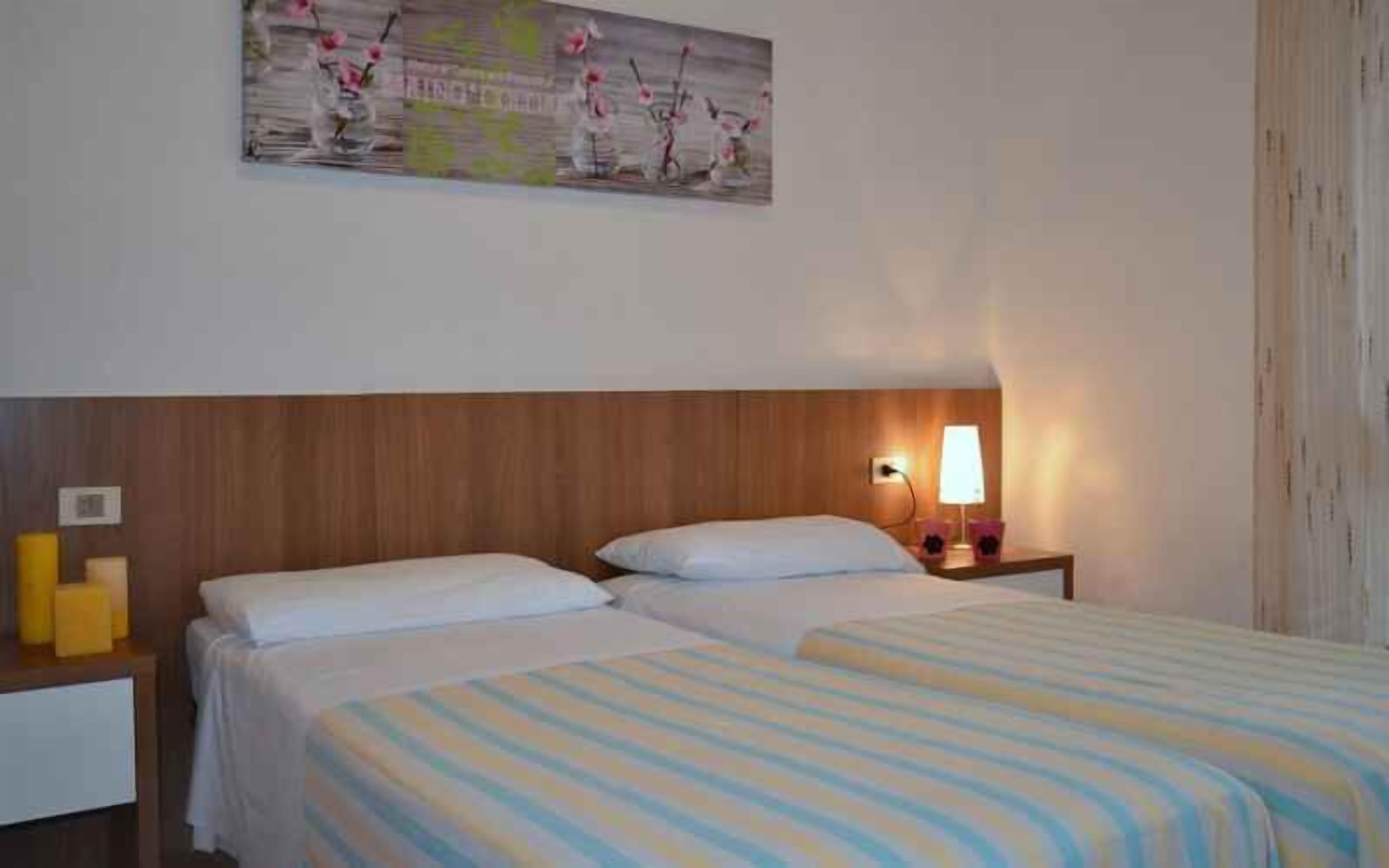 Une chambre d’hôtel avec deux lits, une tête de lit en bois, une table de chevet avec une lampe et un tableau au mur.