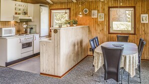 A rustic kitchen with wooden walls, a central island, and a dining area with chairs and a table.