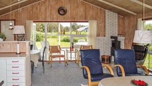 A cozy room with a wooden ceiling, a fireplace, a dining table with chairs, and a view of the outdoors.