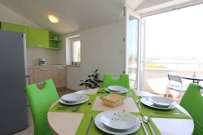 A dining area with a table set for four, surrounded by green chairs, and a view of the outdoors through a glass door.