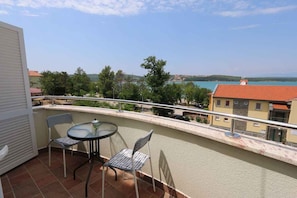 A balcony with a table and two chairs, overlooking a coastal area with buildings and trees.