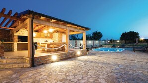 A stone patio with a pool, a covered outdoor kitchen, and lounge chairs. - Luxurious home in Gorica (Gorica)