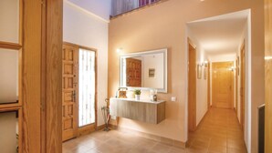 Un couloir avec des portes en bois, un miroir et une petite armoire contenant des objets décoratifs.