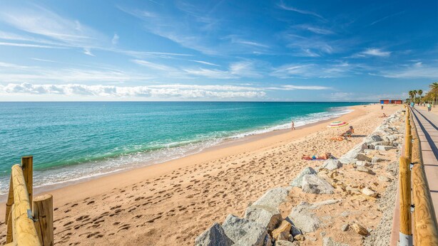 Une plage avec une promenade en bois, un ciel bleu clair et une mer calme.