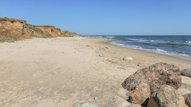 Une plage de sable avec des affleurements rocheux et un ciel bleu dégagé.