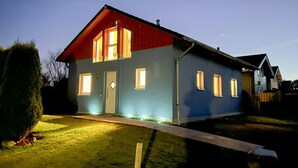 Une maison à deux étages avec un toit rouge et des murs bleus, dotée de nombreuses fenêtres et d’une porte d’entrée bien visible.