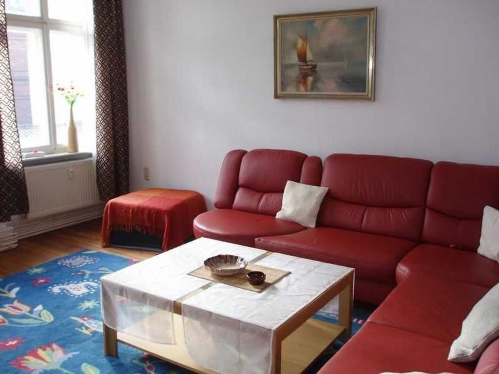 Un soggiorno con un divano rosso, un tavolino da caffè e un quadro appeso al muro.