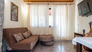 A cozy living room with a brown sofa, patterned ottoman, stone wall, and a television mounted on the wall. - Lovely apartment in Jadrija with WiFi (Jadrija)