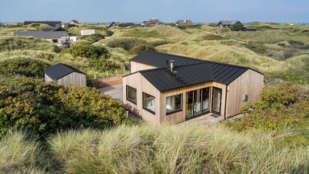 Una casa moderna con una amplia terraza, rodeada de dunas y vegetación naturales.