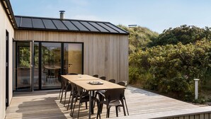 Un área de comedor al aire libre moderna con terraza de madera, una mesa larga y sillas.