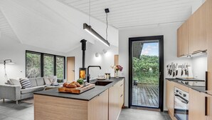 Una cocina moderna con una isla central, estufa integrada y un amplio ventanal con vistas al verdor.