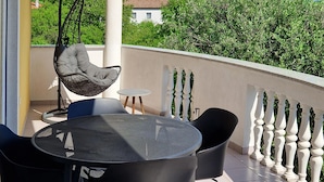 Un balcón con una mesa redonda y sillas, una silla colgante y una barandilla blanca.