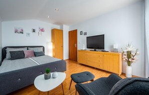 Et moderne soveværelse med seng, fjernsyn, kommode og et lille bord med to potteplanter.