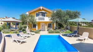 Una casa de dos pisos con piscina, mobiliario exterior y jardín.