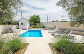 En swimmingpool med liggestole, et mindre skur og grøn bevoksning omkring.