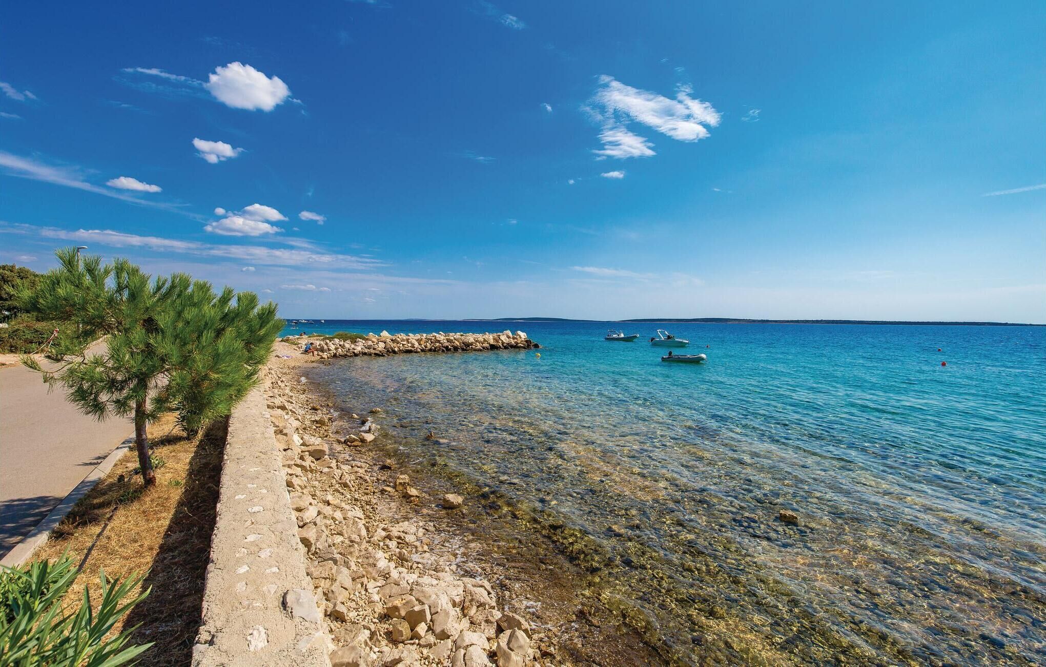 Una strada costiera con un litorale roccioso, acqua blu cristallina e barche.