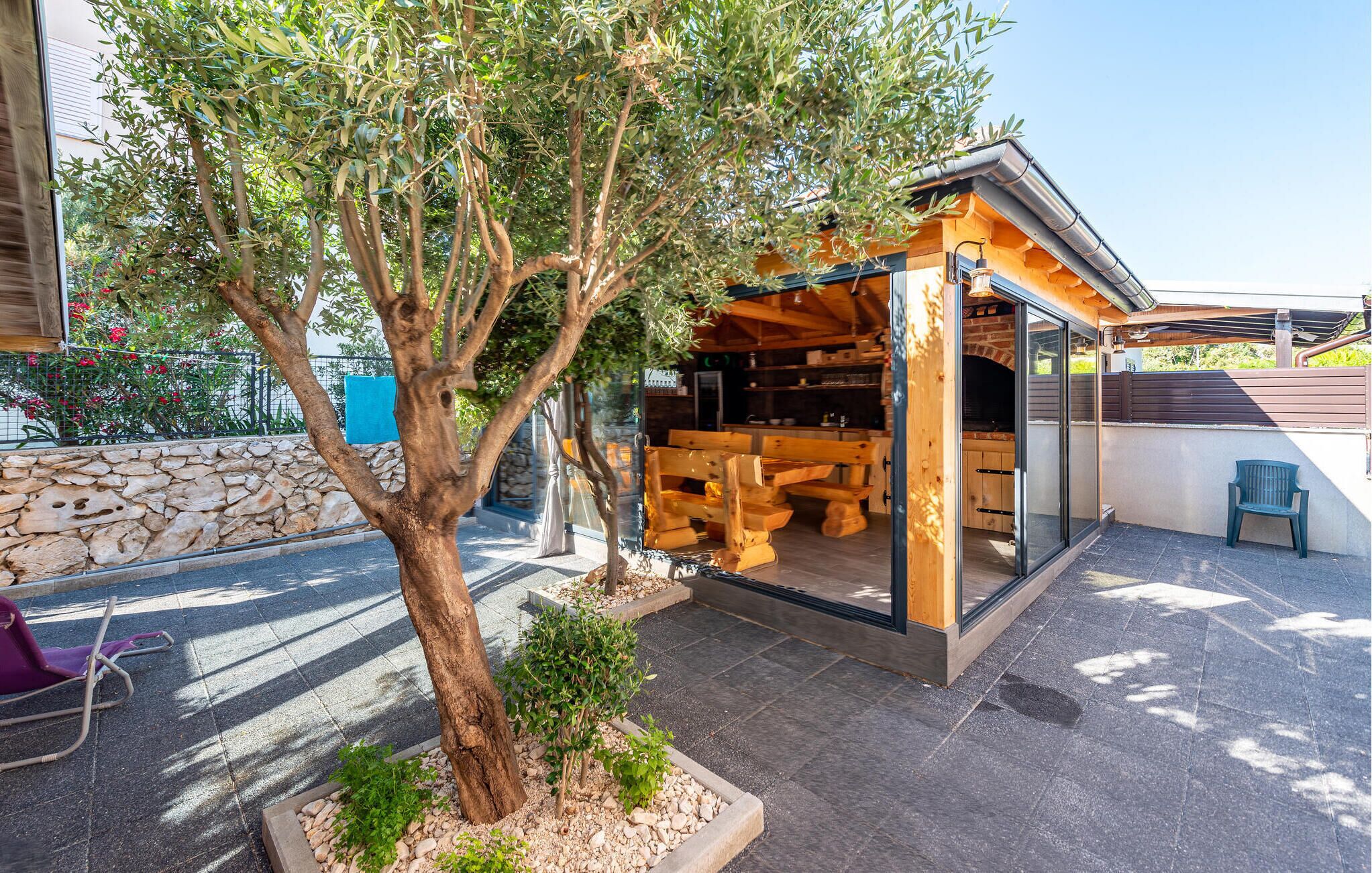A wooden outdoor dining area with a stone wall and a tree.