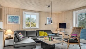 A modern living room with a sectional sofa, a coffee table, a wicker chair, and artwork on the walls. - Beach front home in Hvide Sande with sauna (Hvide Sande)